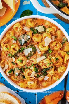 a bowl of pasta with spinach, cheese and bread on a blue tablecloth