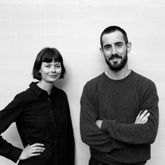 two people standing next to each other in front of a white wall with their arms crossed