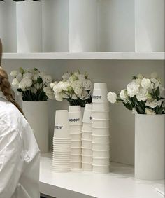 a woman standing in front of white vases filled with flowers