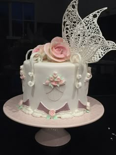 a white cake with pink flowers on top and a butterfly decoration around the edges is sitting on a table