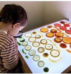 a young boy looking at an array of fruit on a white table with oranges and kiwi slices