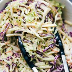 a white bowl filled with coleslaw and two serving spoons