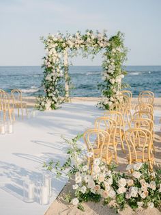 an outdoor ceremony set up on the beach with chairs and flowers in front of the ocean