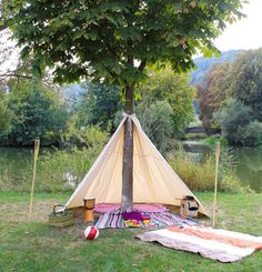 a teepee sitting on top of a lush green field next to a lake and forest