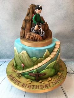 a birthday cake with a boy riding a bike on it's side and mountains in the background