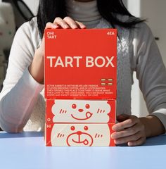 a woman holding up a tart box on top of a table