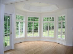 an empty room with large windows and wooden floors in the center is seen from the doorway