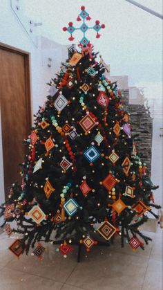 a decorated christmas tree in a room with tile flooring and white walls, surrounded by multi - colored ornaments