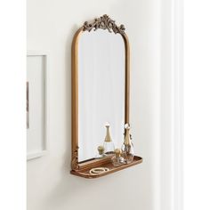 a mirror on the wall above a shelf with vases and an ornate candle holder