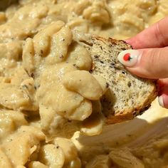 a hand holding a piece of bread with macaroni and cheese on it in a bowl