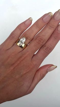 a woman's hand with gold and white manicured nails holding a diamond ring