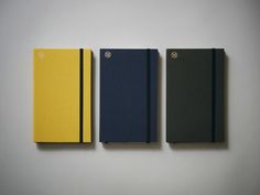 three notebooks lined up in different colors on a white surface, one yellow and the other blue