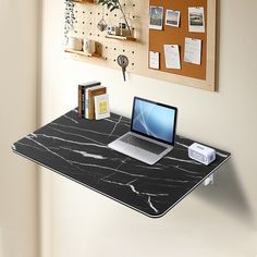 a laptop computer sitting on top of a desk next to a wall mounted cork board