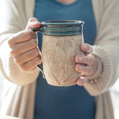 a woman holding a coffee cup with leaves on the side and writing on the inside