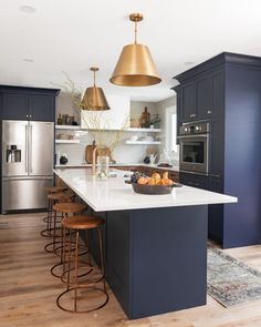 a large kitchen with blue cabinets and gold pendant lights over the island countertop, along with stools