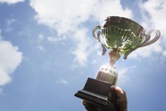 a person holding up a trophy in front of a blue sky with clouds and sun