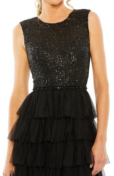 This glamorous gown is designed in a sleeveless silhouette with a lustrous sequin bodice and a gauzy tiered ruffle skirt. Hidden back-zip closure Jewel neck Sleeveless Partially lined 100% polyester Spot clean Imported Asian Owned/Founded Sleeveless Embellished Sequin Tulle Dress, Embellished Sleeveless Sequin Tulle Dress, Evening Tiered Tulle Gown, Tiered Tulle Gown For Evening, Sleeveless Gown With Contrast Sequin For Formal, Tiered Sequin Evening Dress, Tiered Sequin Dress For Evening, Elegant Sequin Dress With Ruffles For Wedding, Glamorous Tiered Evening Dress For Wedding