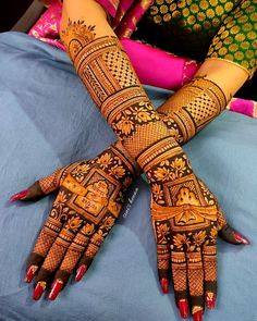 two hands with henna designs on them sitting on top of a blue bed covered in pillows