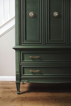 a green armoire sitting on top of a wooden floor next to a stair case