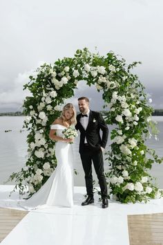 a bride and groom pose for a photo in front of a floral arch at their wedding