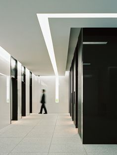 a man walking down a hallway between two black and white walls with light coming from the ceiling