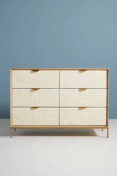 a white dresser sitting on top of a floor next to a blue wall with polka dots