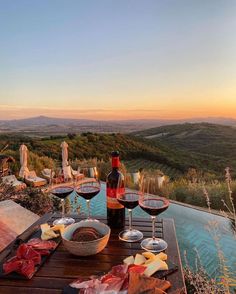 two glasses of wine are sitting on a table with food and drinks in front of an outdoor swimming pool