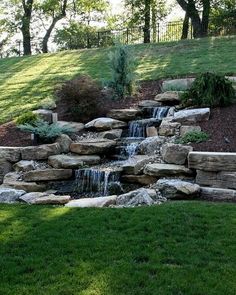 there is a small waterfall in the middle of this garden with rocks and grass around it