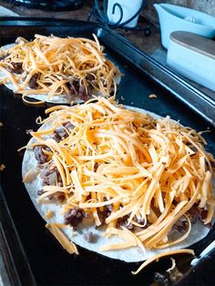 two uncooked pizzas sitting on top of an oven pan covered in cheese