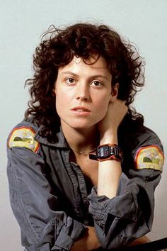 a woman with curly hair wearing a watch and looking off to the side while leaning on her hand