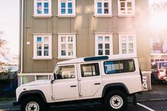 a white jeep parked in front of a tall building with windows on it's side