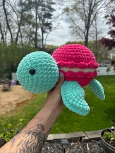 a hand holding a small crocheted turtle toy in front of a grassy area