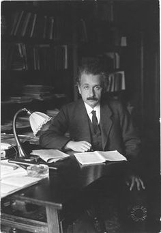 a man in a suit sitting at a desk with papers and a lamp on it