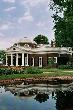 a large brick house sitting on top of a lush green field next to a lake