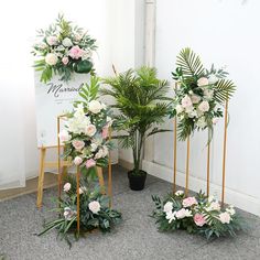 three potted plants in front of a sign and two chairs with flowers on them