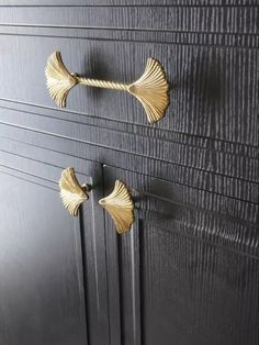 two gold handles on a black cabinet with wood grained panels and brass leaf knobs