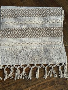 a white rug with tassels and fringe on top of a wooden floor next to a wood floor