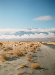 an empty road in the middle of nowhere with mountains in the backgrouund