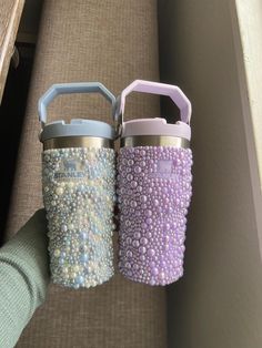 two purple and blue insulated cups sitting next to each other on top of a couch