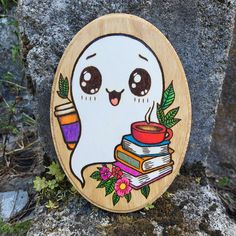 a wooden plaque with a ghost holding books and a cup on it's face