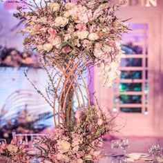 a tall vase filled with lots of pink flowers on top of a table next to wine glasses