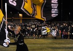 the football team is running onto the field with their flags in hand and fans behind them