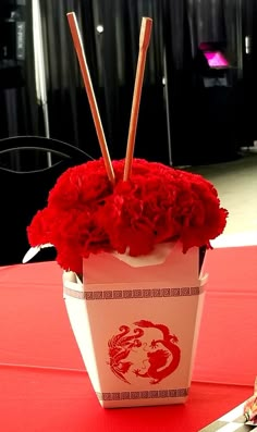 red flowers in a white container with chopsticks sticking out of it on a table