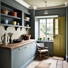 a kitchen with blue cabinets and wooden counter tops next to a yellow door in front of a window