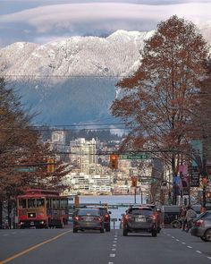 cars are driving down the street in front of snow - capped mountains and city buildings