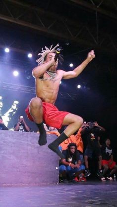 a shirtless man is jumping in the air with his legs spread out while people look on