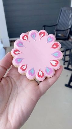 a hand holding a pink flower shaped cookie in front of a patio with rocking chairs