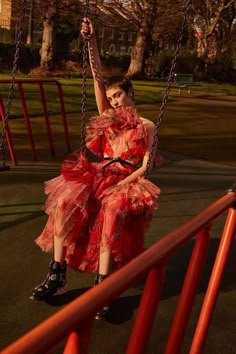 a woman in a red dress is sitting on a swing