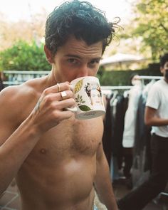 a shirtless man drinking from a coffee cup