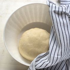 a white bowl filled with dough sitting on top of a counter next to a blue and white towel